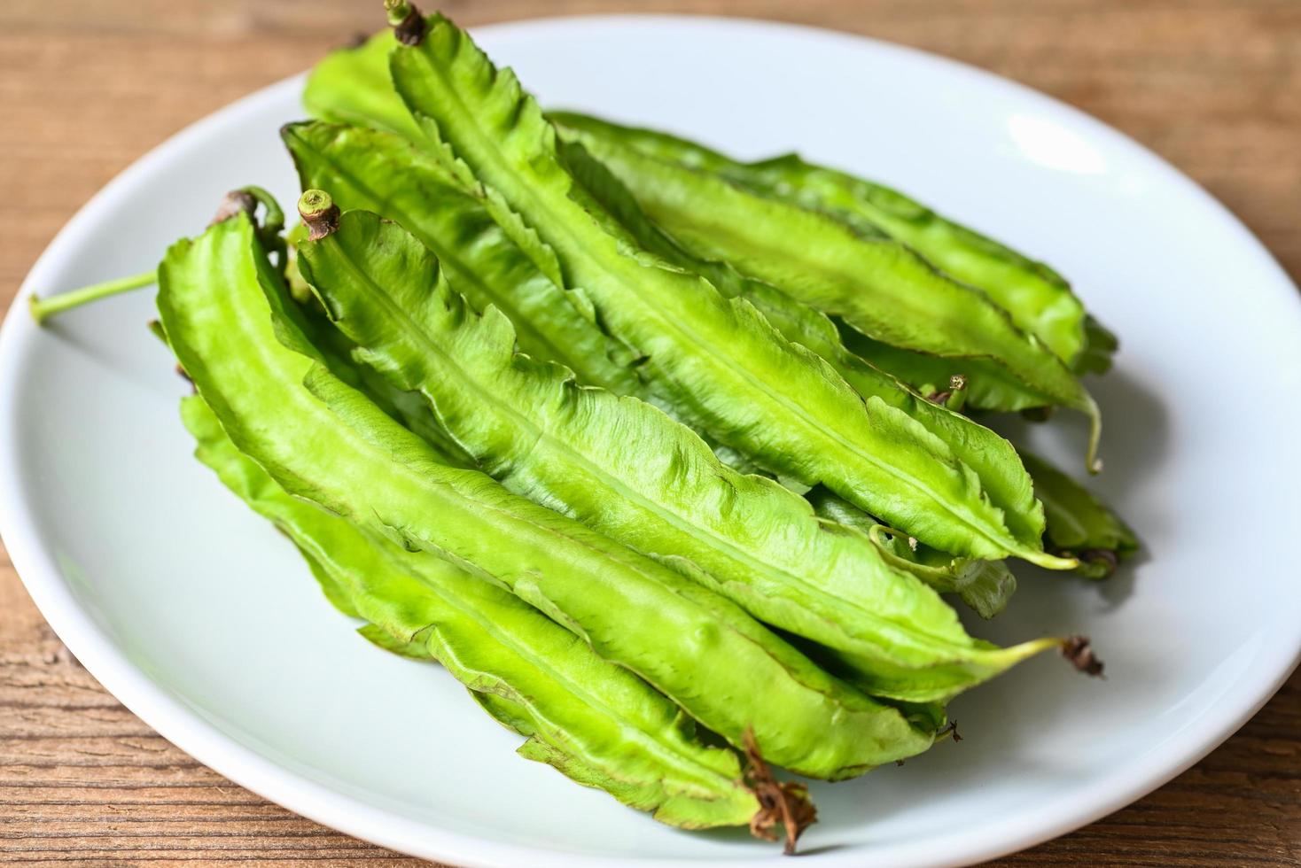 Haricot ailé sur fond de plaque blanche, psophocarpus tetragonolobus - haricots verts ailés ou à quatre angles photo