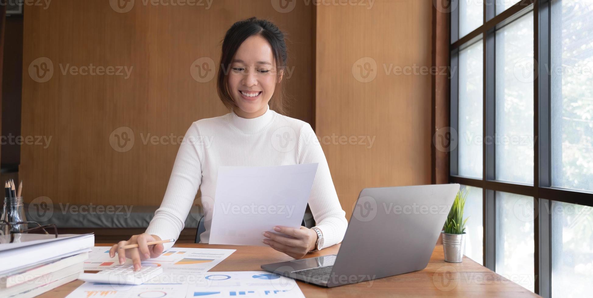 portrait d'une jeune femme asiatique pigiste à la main travaille son travail sur une tablette informatique dans un bureau moderne. faire un rapport d'analyse comptable sur les données d'investissement immobilier, le concept de systèmes financiers et fiscaux. photo