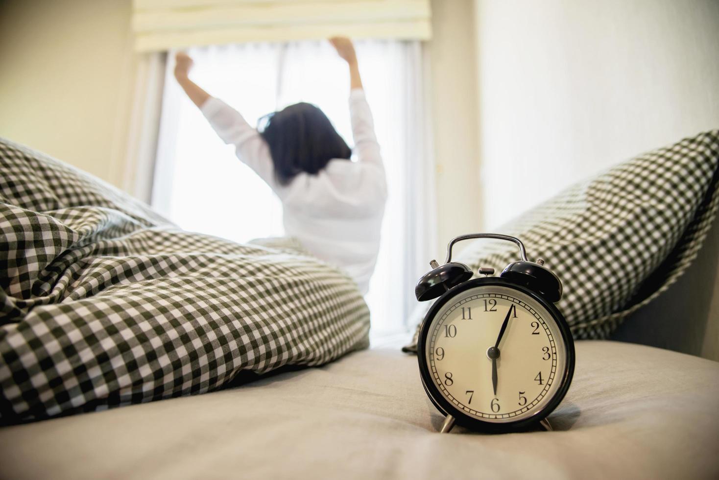 femme endormie atteignant tenant le réveil le matin avec un réveil tardif - concept de la vie quotidienne à la maison photo