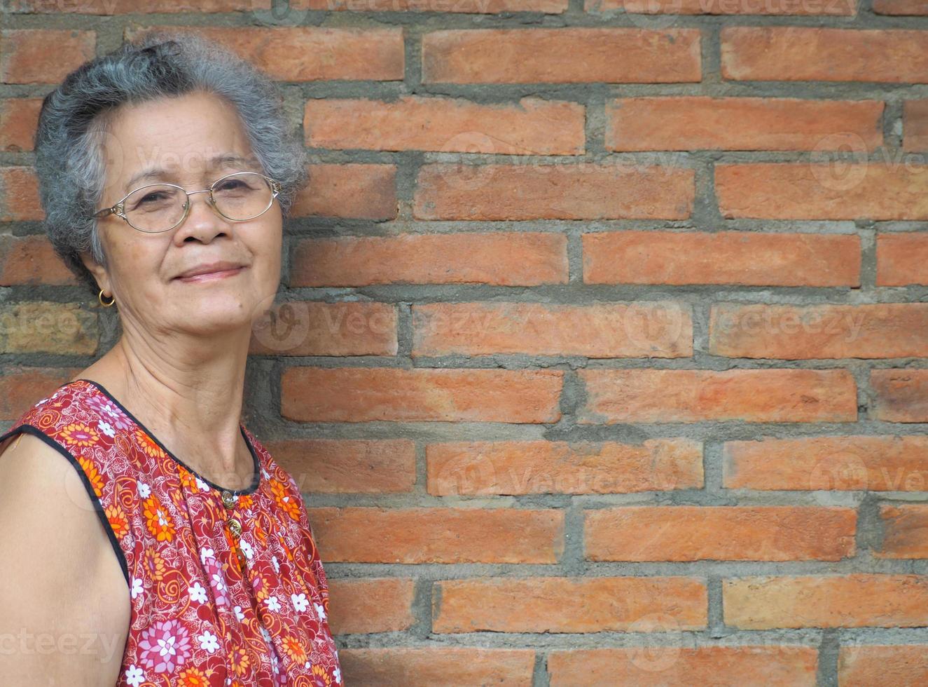 une femme asiatique âgée debout et regardant la caméra avec un fond de mur de briques photo