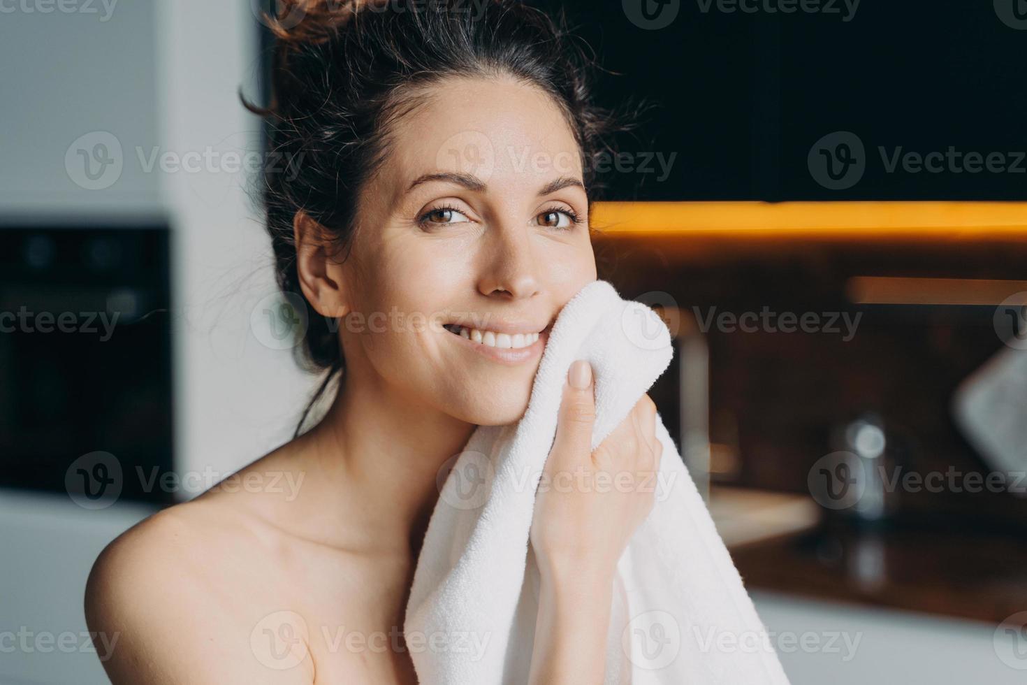 une fille européenne s'essuie le visage avec une serviette après le lavage. jeune femme brune prend une douche à la maison. photo