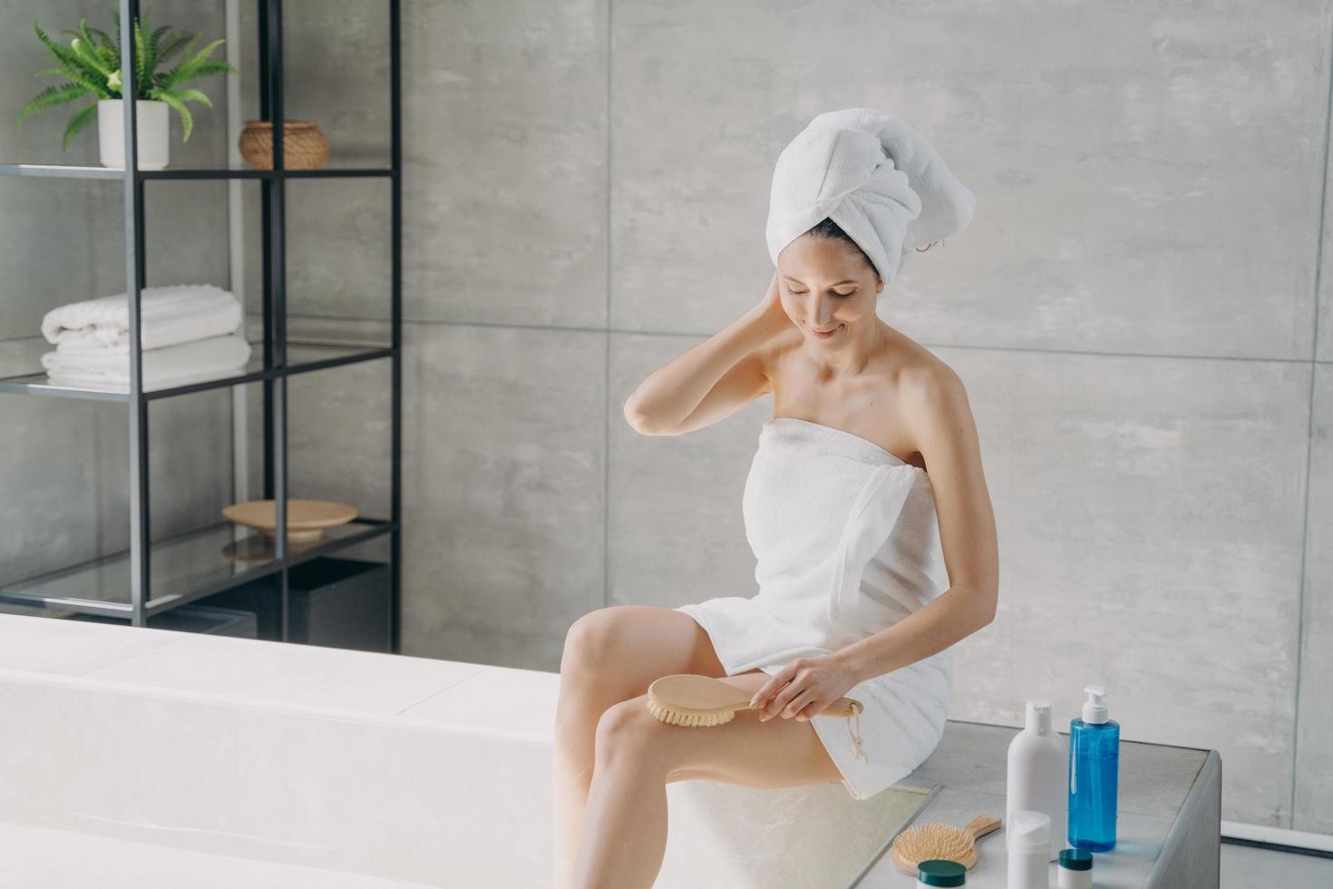 jolie fille caucasienne fait un massage du corps avec une brosse dans la salle de bain. routine de soins du corps du matin. photo