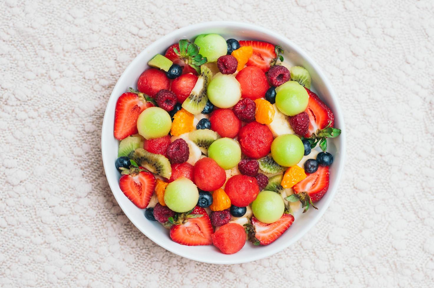 salade de fruits frais sains dans un bol. tranches de fraise, framboise, kiwi, mandarines, myrtille sur assiette. fruits délicieux. plat végétarien. baies mûres. photo