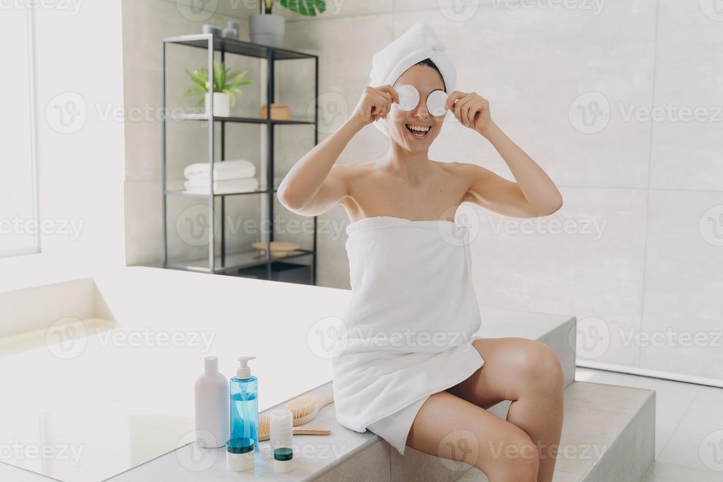 une femme heureuse s'amuse à appliquer du toner pour le visage avec des disques de coton. dame assise sur la baignoire et relaxante. photo