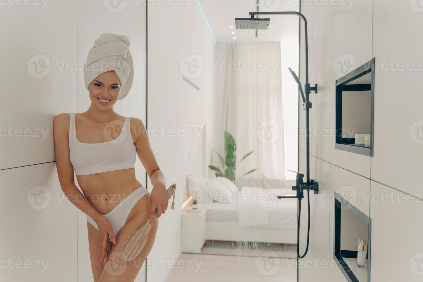jolie jeune femme faisant un massage des jambes sèches avec une brosse organique en bois photo