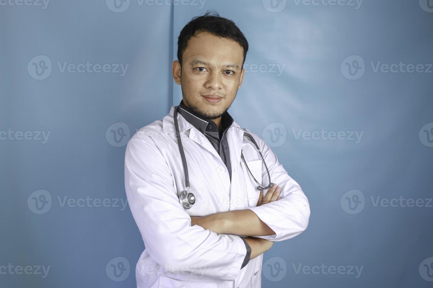 portrait d'un médecin de sexe masculin attrayant et confiant, bras croisés souriants et amicaux, porter un stéthoscope de blouse de laboratoire blanc isolé sur fond bleu photo