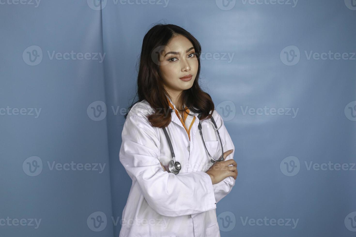 portrait d'une jolie femme médecin confiante, amicale et souriante bras croisés porter un stéthoscope de blouse de laboratoire blanc isolé sur fond bleu photo
