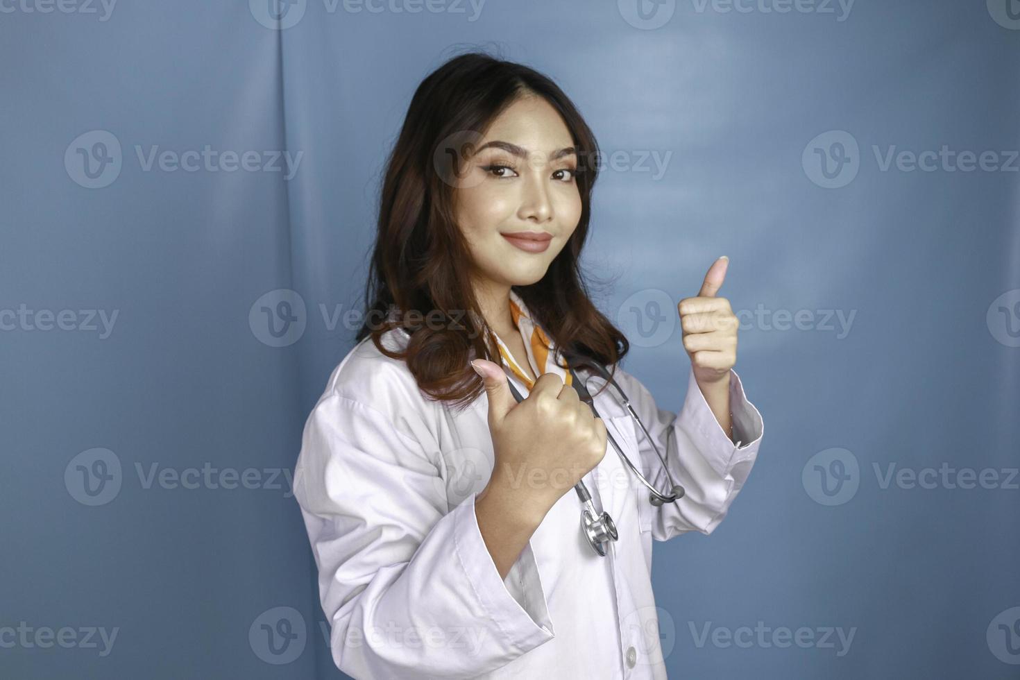 portrait d'une jeune femme médecin asiatique, un professionnel de la santé sourit et montre le pouce levé ou le signe ok isolé sur fond bleu photo