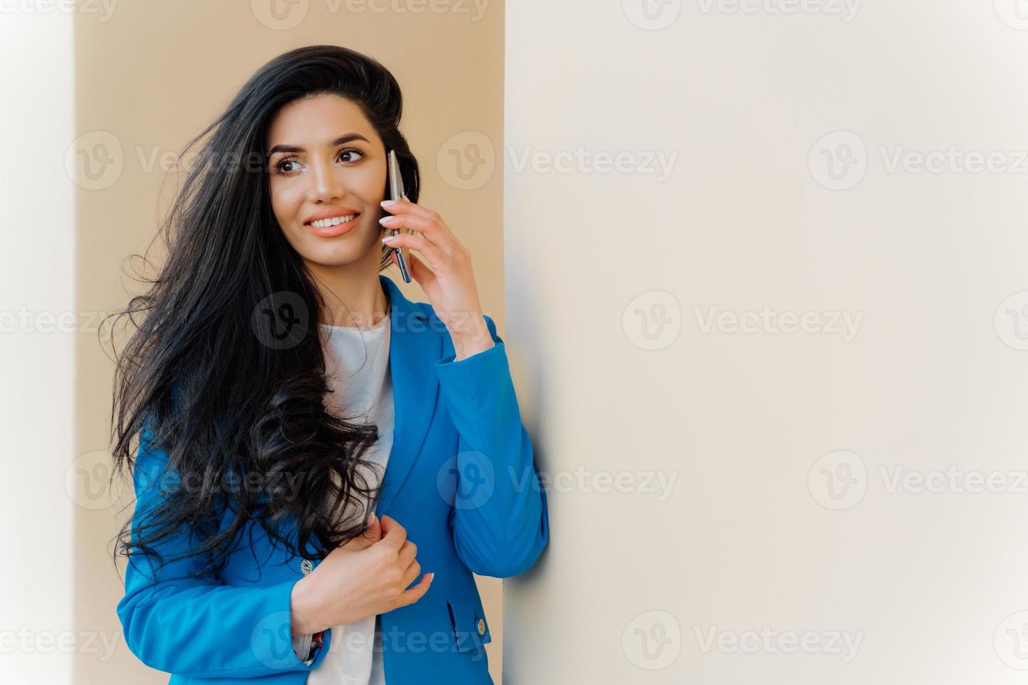 une femme d'affaires européenne joyeuse parle de ses réalisations, profite de bonnes nouvelles au travail, porte une élégante veste bleue, regarde joyeusement de côté. une employée heureuse se réjouit de la prospérité de sa carrière, utilise le cellulaire photo