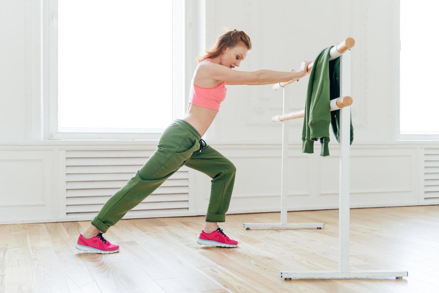 sport, loisirs, concept de flexibilité. une femme forte et motivée fait de la planche, se penche à la barre de ballet, s'étire avant les exercices prépare les muscles ou les biceps pour un entraînement intensif. instructeur d'aérobic à l'intérieur photo