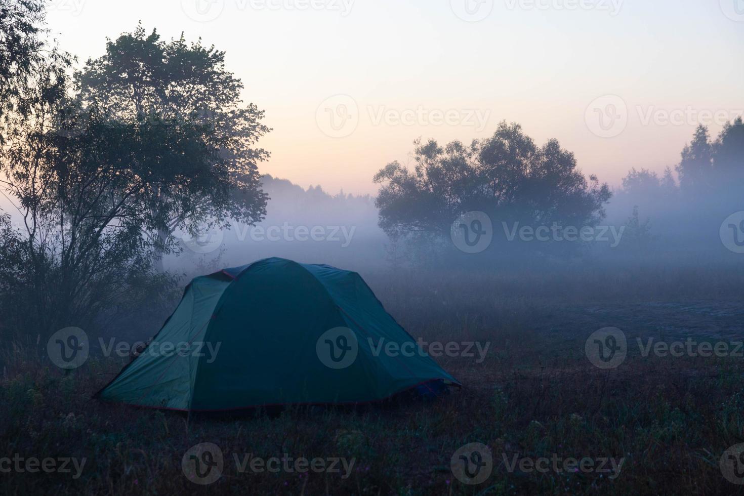 tente touristique verte au bord de la rivière au lever du soleil, avec brouillard d'automne matinal sur l'eau. paysage touristique en plein air. photo