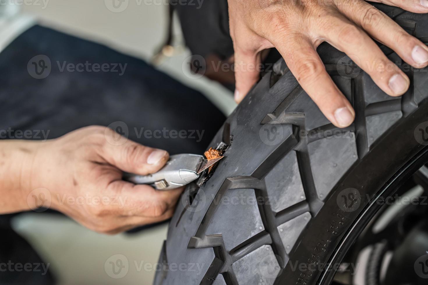 le pilote utilise un kit de bouchon de pneu et essaie de réparer un trou dans le flanc du pneu, répare un pneu crevé de moto dans le garage. concept d'entretien et de réparation de moto photo