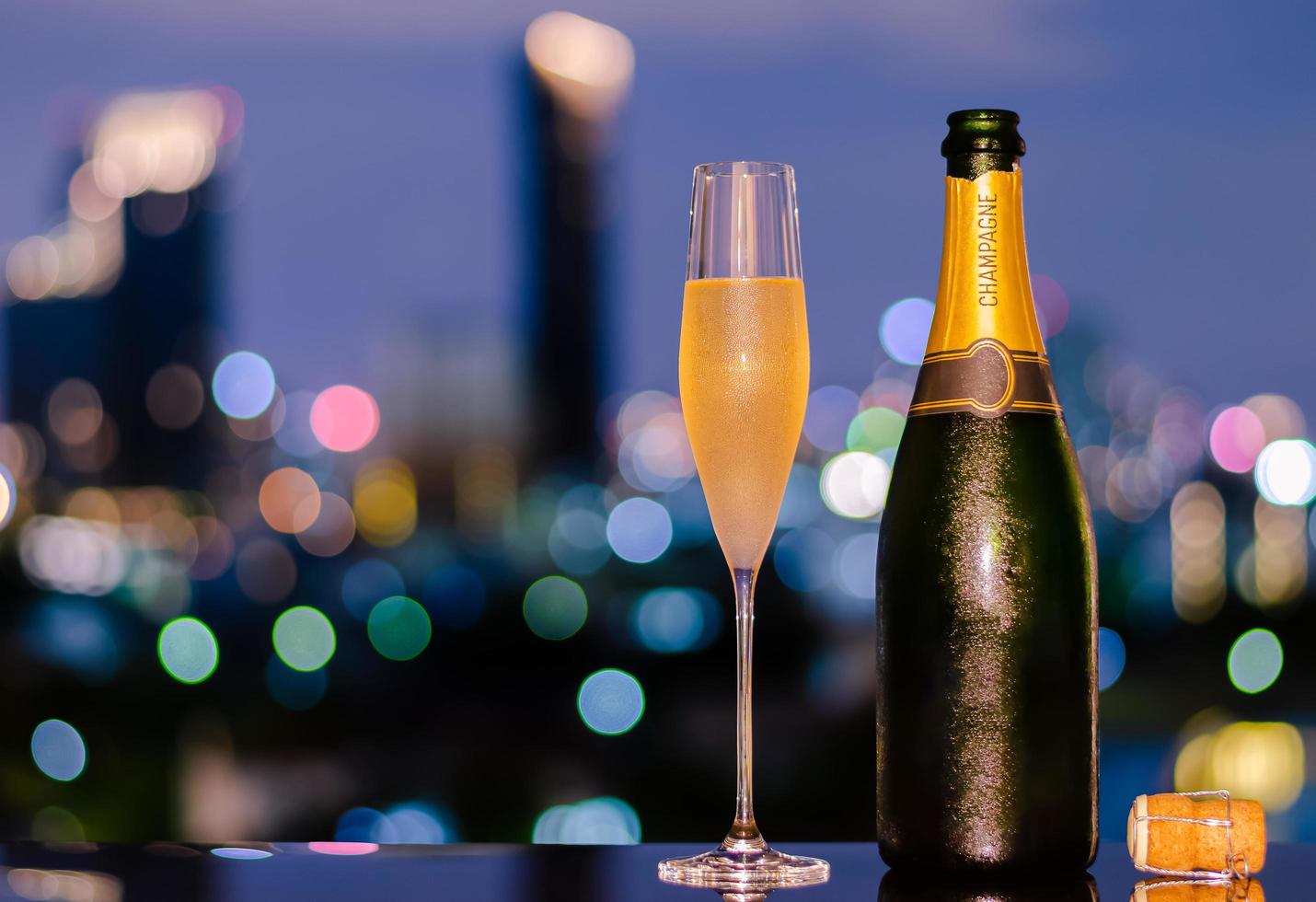 un verre avec de la vapeur de champagne froid avec une bouteille et du liège sur fond de lumières bokeh colorées de la ville. photo