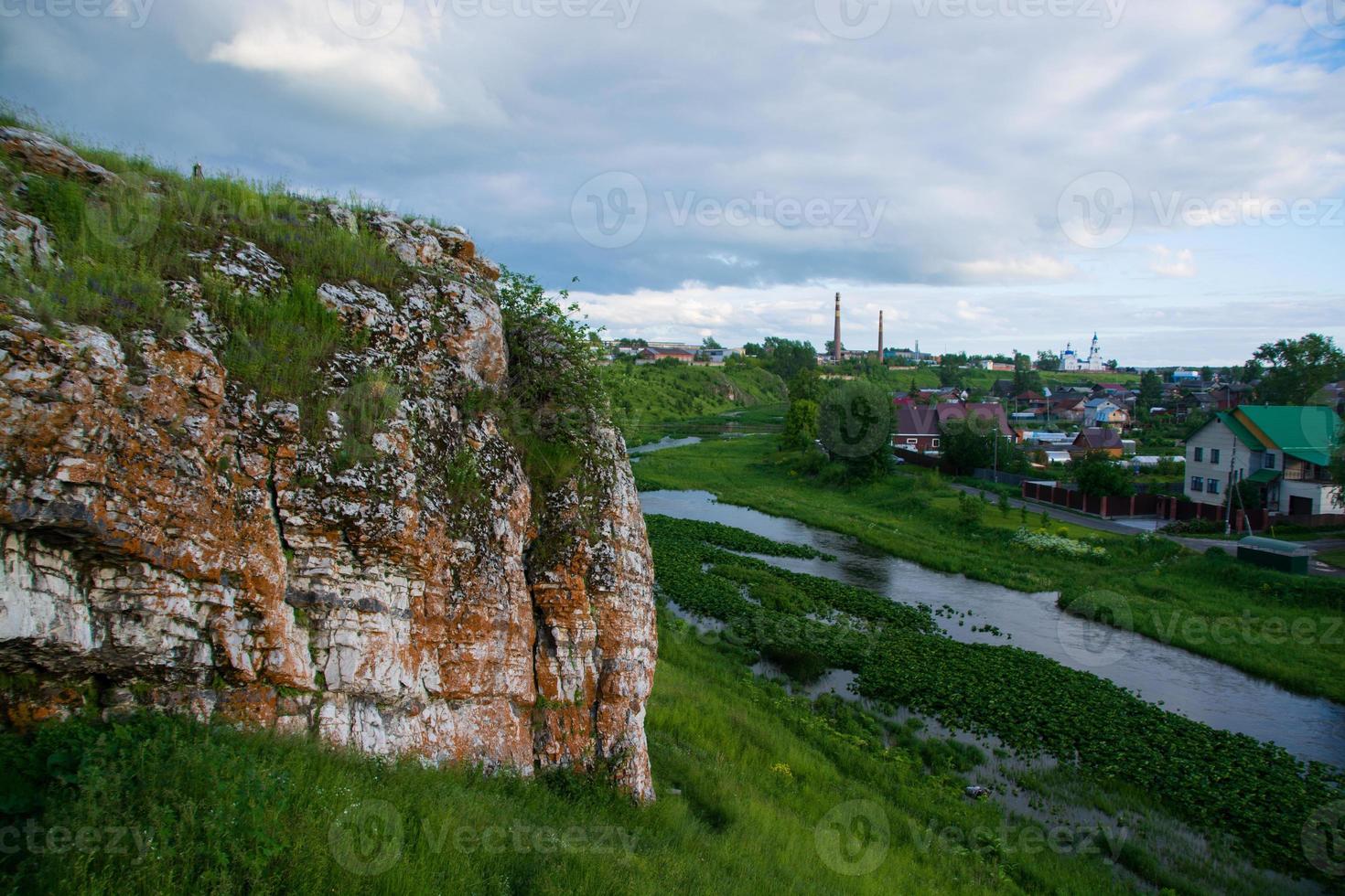 un rocher près de la rivière et du village sur fond de ciel coucher de soleil. photo