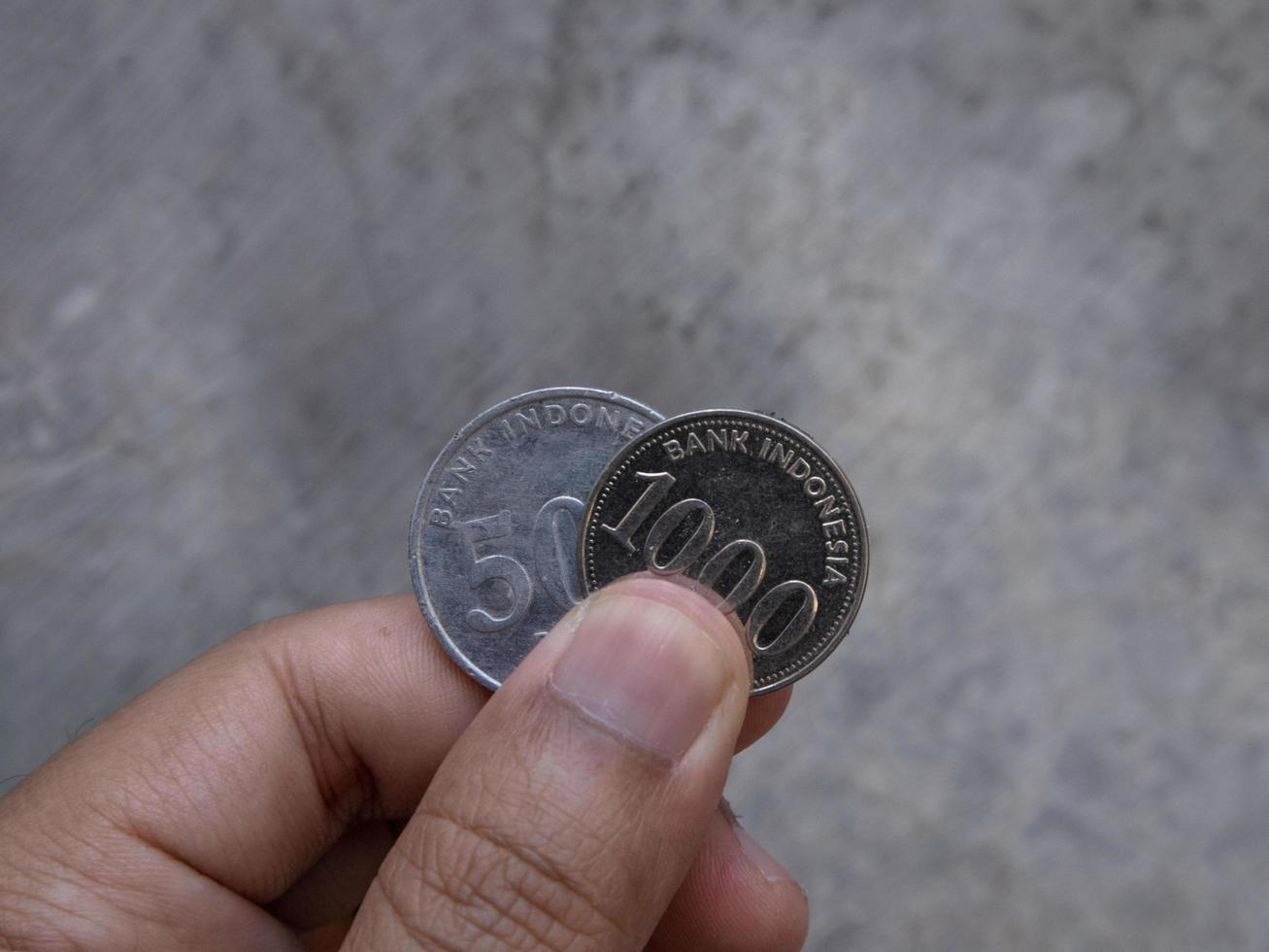 un homme tenant deux pièces de 500 et 1000 roupies en monnaie indonésienne photo