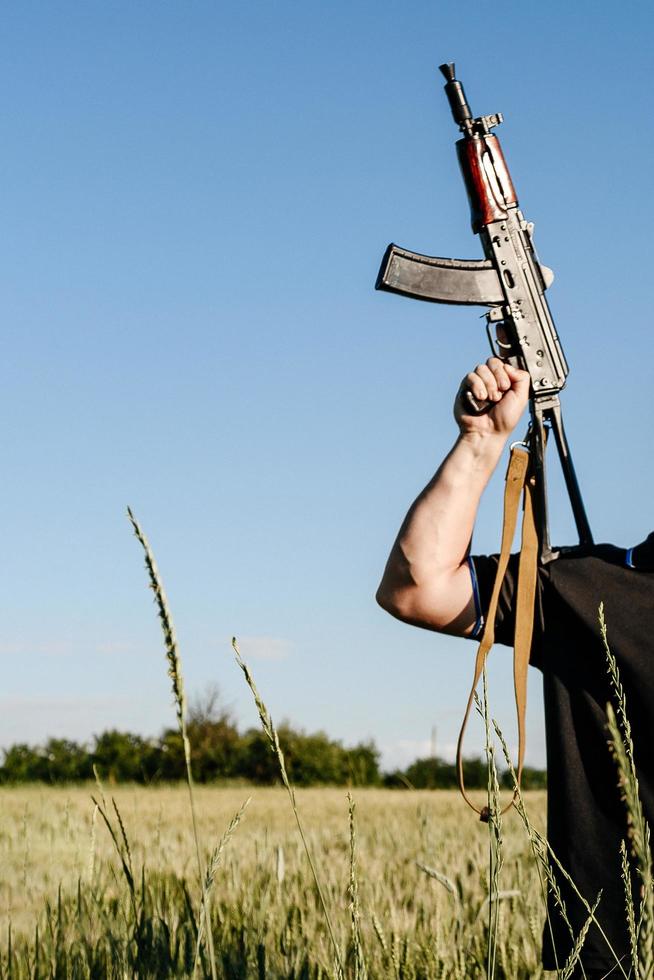 un soldat avec un fusil d'assaut militaire de combat ak 74 se tient dans un champ, des champs de blé ukrainiens et la guerre. photo