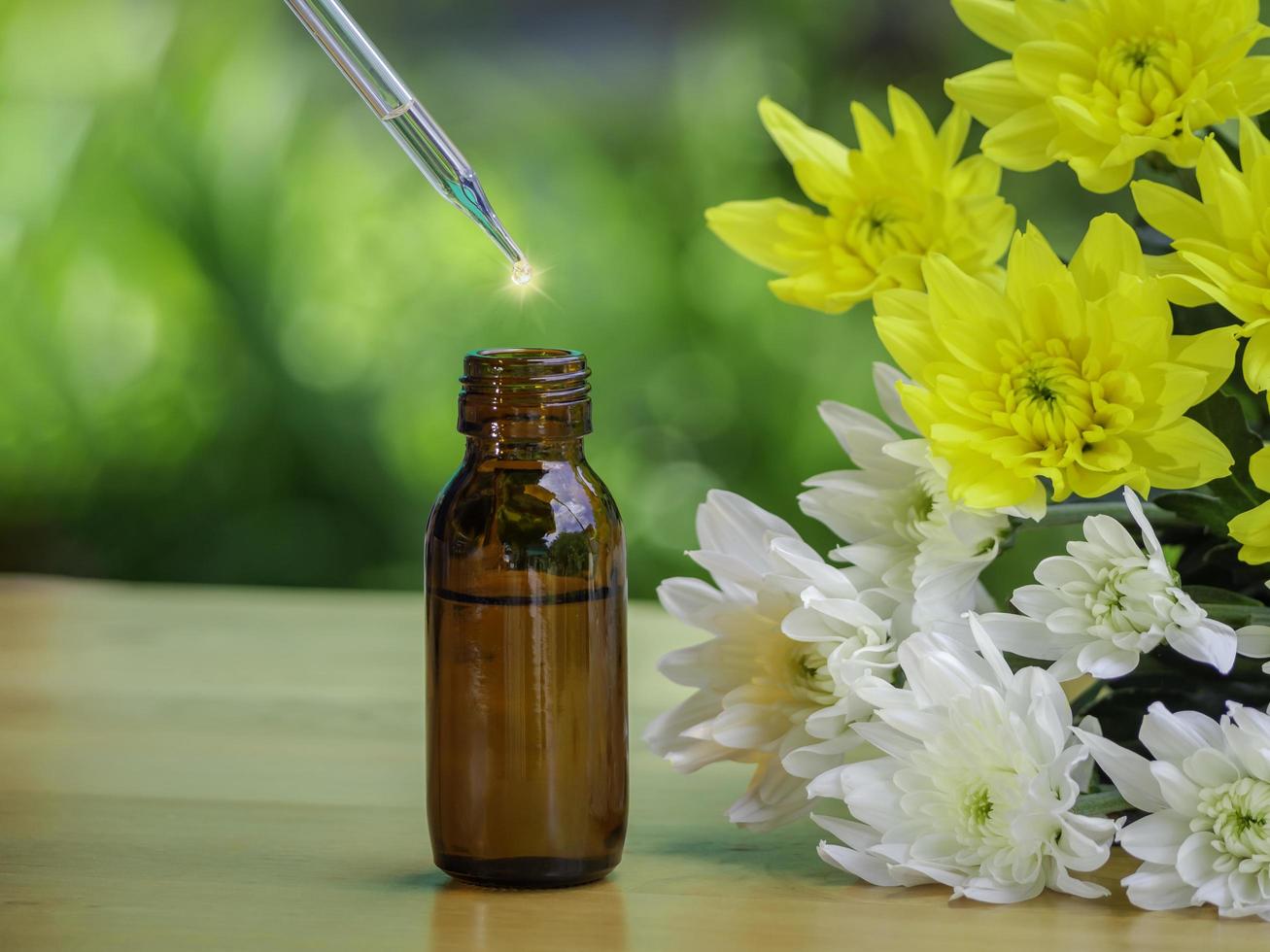 l'extrait d'huiles essentielles et les herbes de fleurs médicales près de la fleur blanche et jaune sur une table en bois. l'huile essentielle bio médecine alternative bio, flacon marron. photo