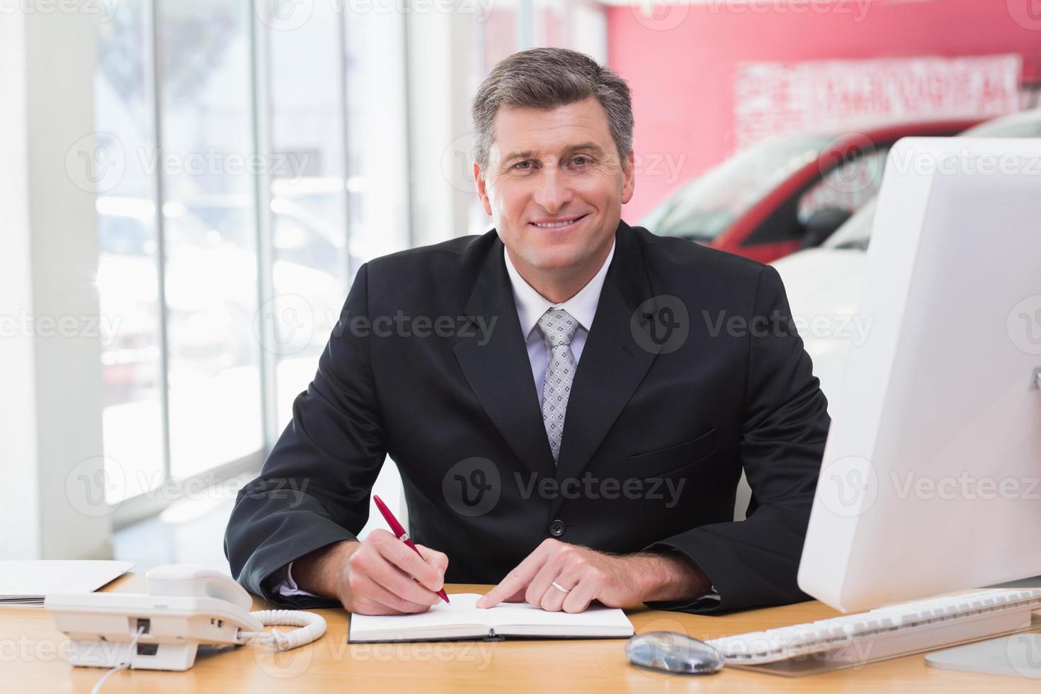 homme d'affaires souriant, écrivant sur le presse-papiers à son bureau photo