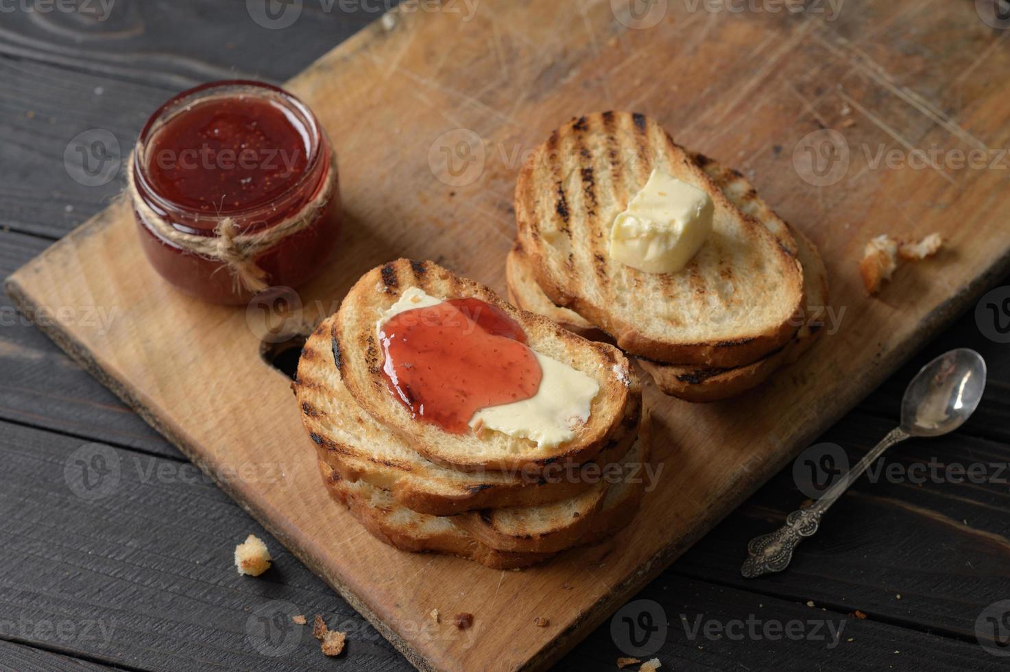 pain grillé avec de la confiture de fraises maison et sur une table rustique avec du beurre pour le petit déjeuner ou le brunch. photo