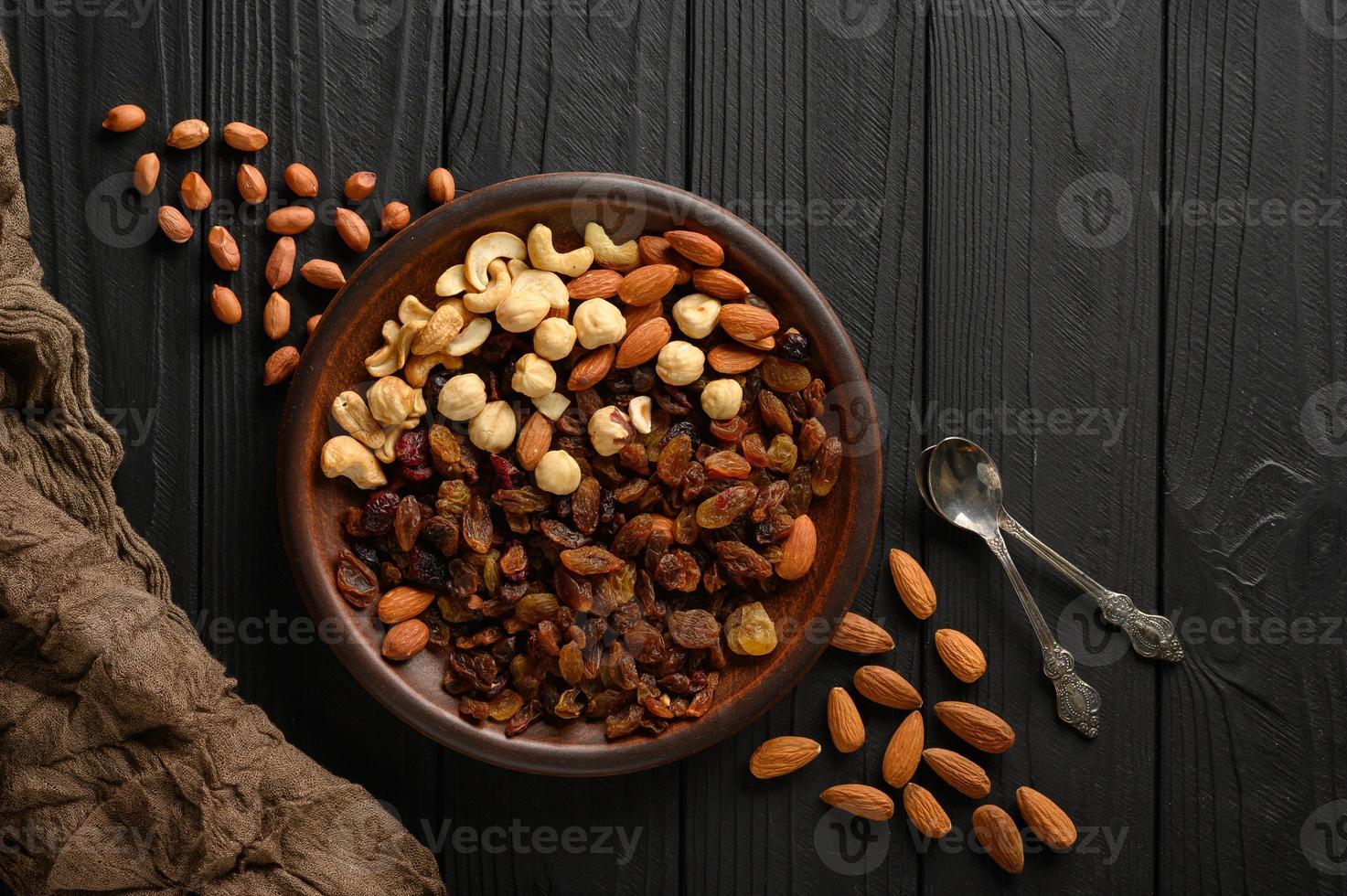 noisette, noix de cajou, raisins secs, amandes, cacahuètes, noix dans des cuillères en argent sur fond rustique photo