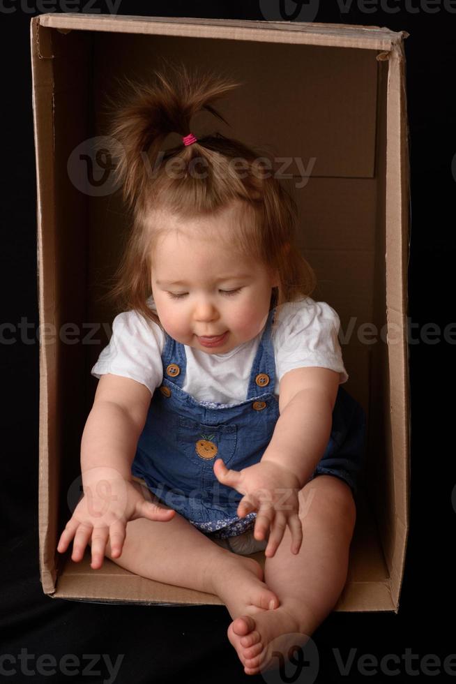 heureuse petite fille assise dans une boîte en carton et s'amusant photo