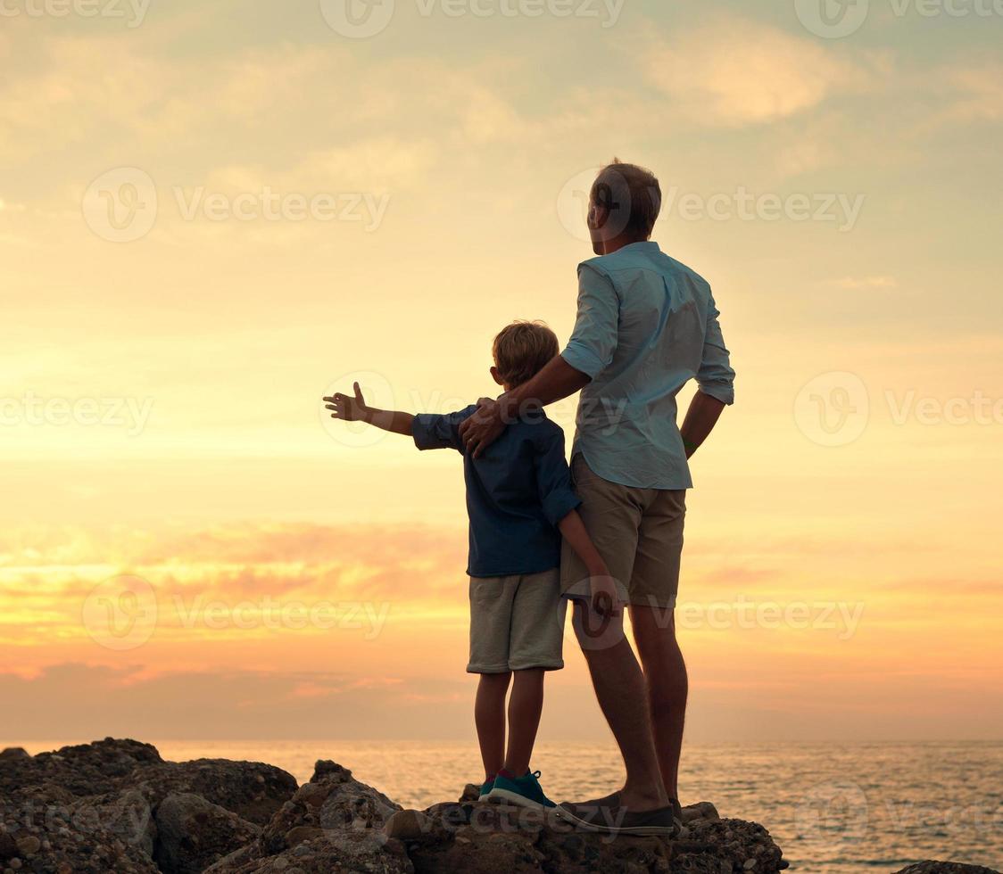 père et fils à la recherche sur le coucher du soleil à la mer photo
