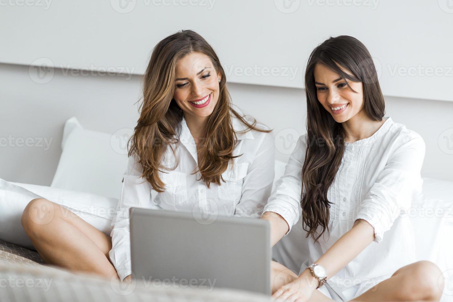 deux belles femmes à l'aide d'un ordinateur portable au lit photo