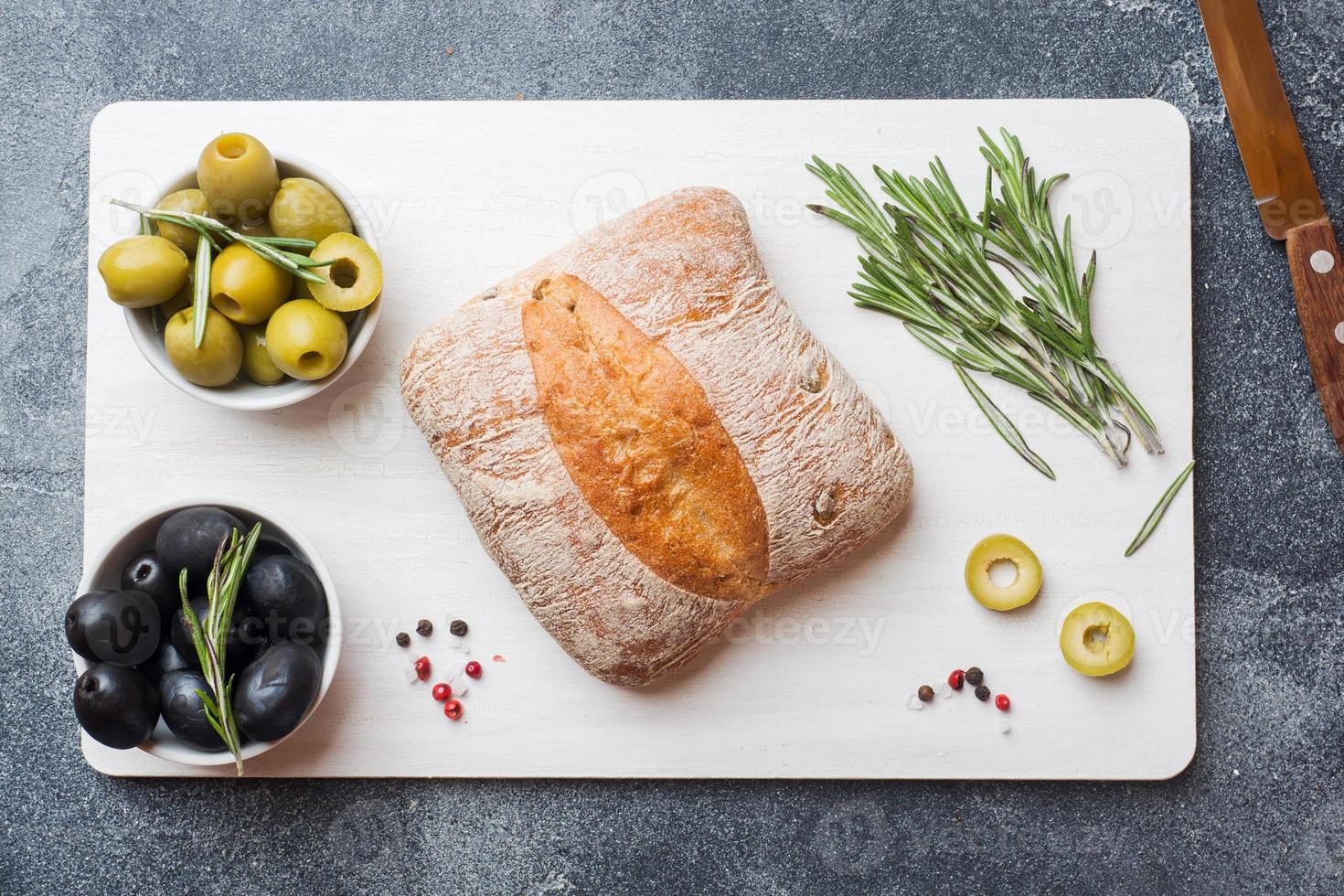 pain ciabatta italien aux olives et au romarin sur une planche à découper. fond de béton foncé. photo