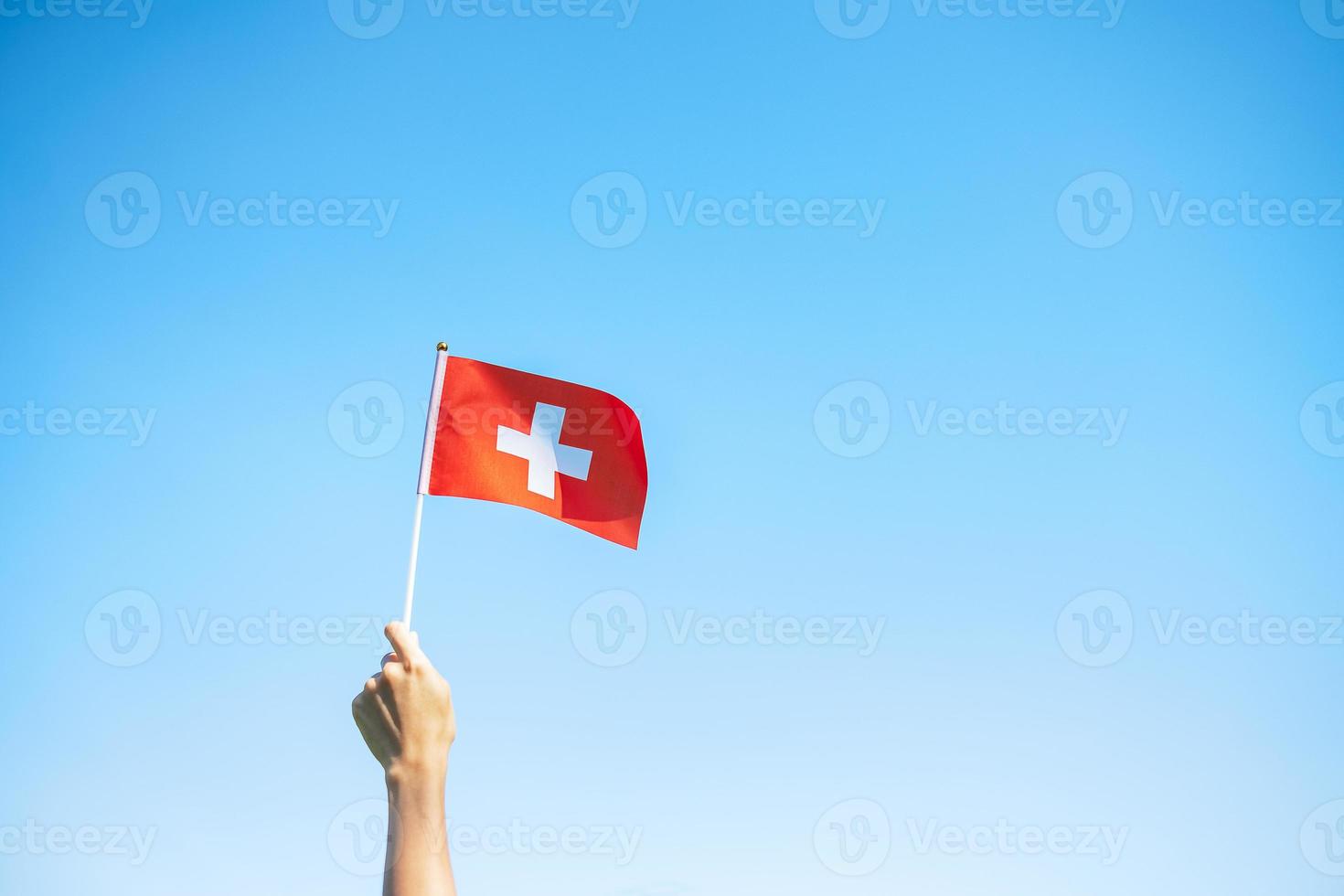 main tenant le drapeau suisse sur fond de ciel bleu. fête nationale suisse et concepts de célébration heureuse photo