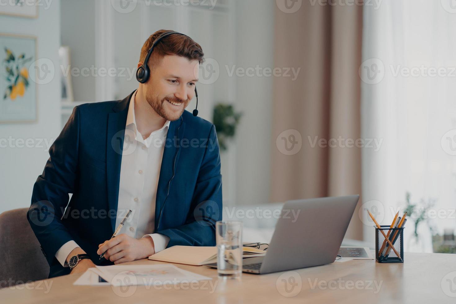 souriant heureux homme d'affaires prospère pratique la conférence en ligne a une réunion à distance avec des collègues porte un casque concentré sur un ordinateur portable porte des vêtements formels. concept de travail indépendant. photo