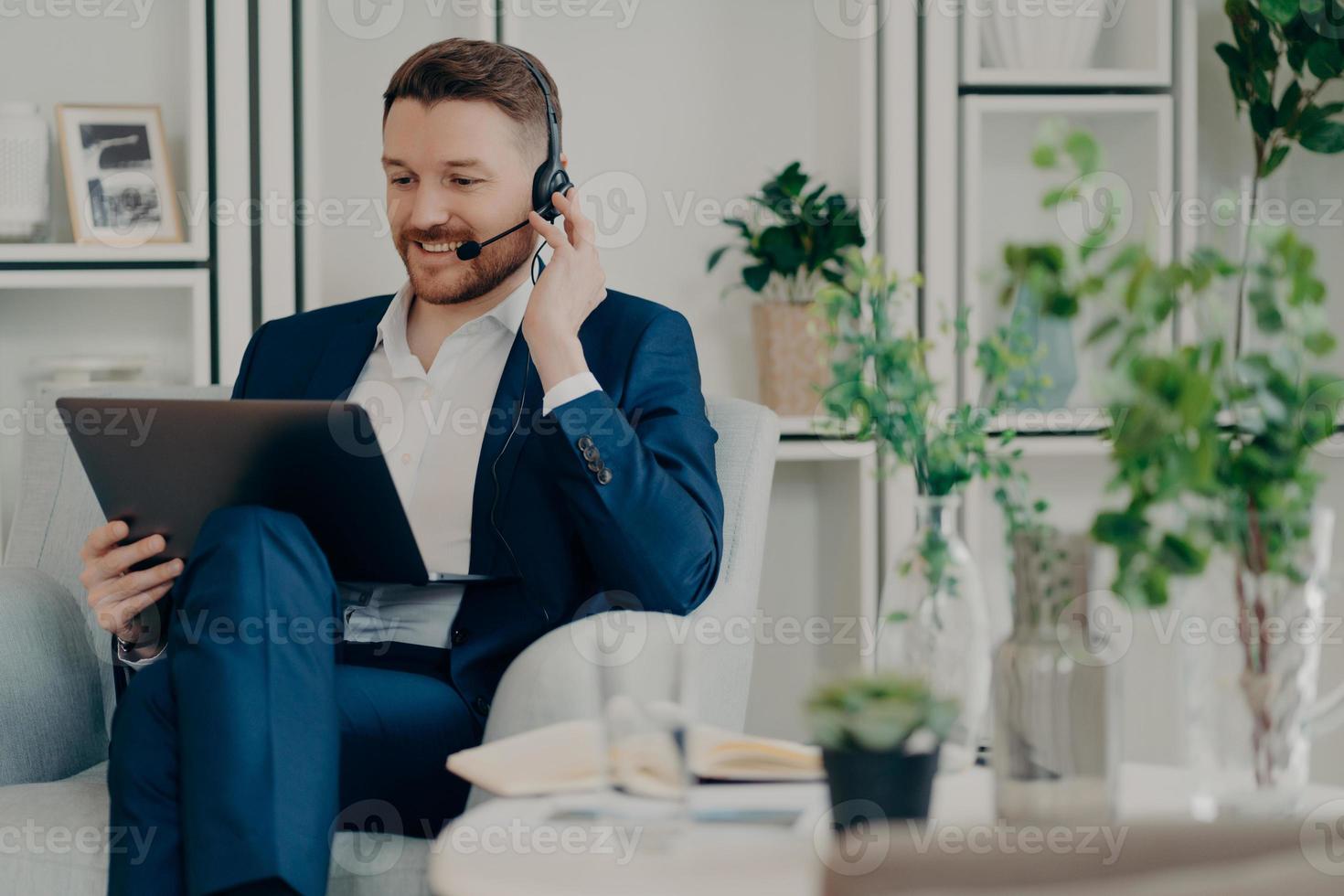 journée de travail indépendante. un homme joyeux et occupé le directeur travaille loin de chez lui en ligne passe un appel vidéo via un ordinateur portable et un casque discute des problèmes de travail avec un partenaire commercial analyse les statistiques photo