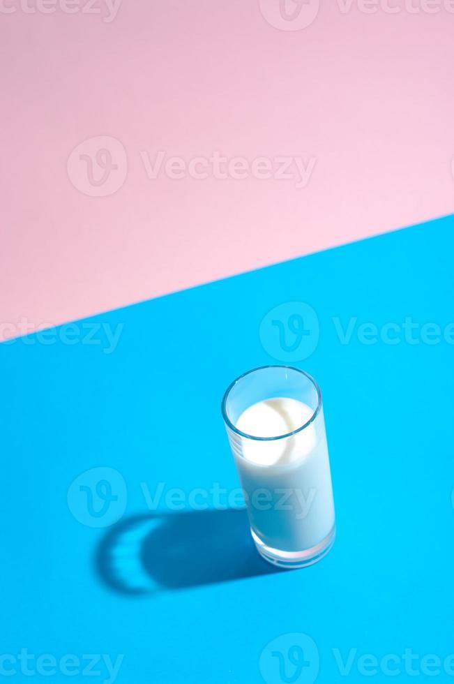 verre de lait avec une ombre dure sur fond bleu et rose. photo