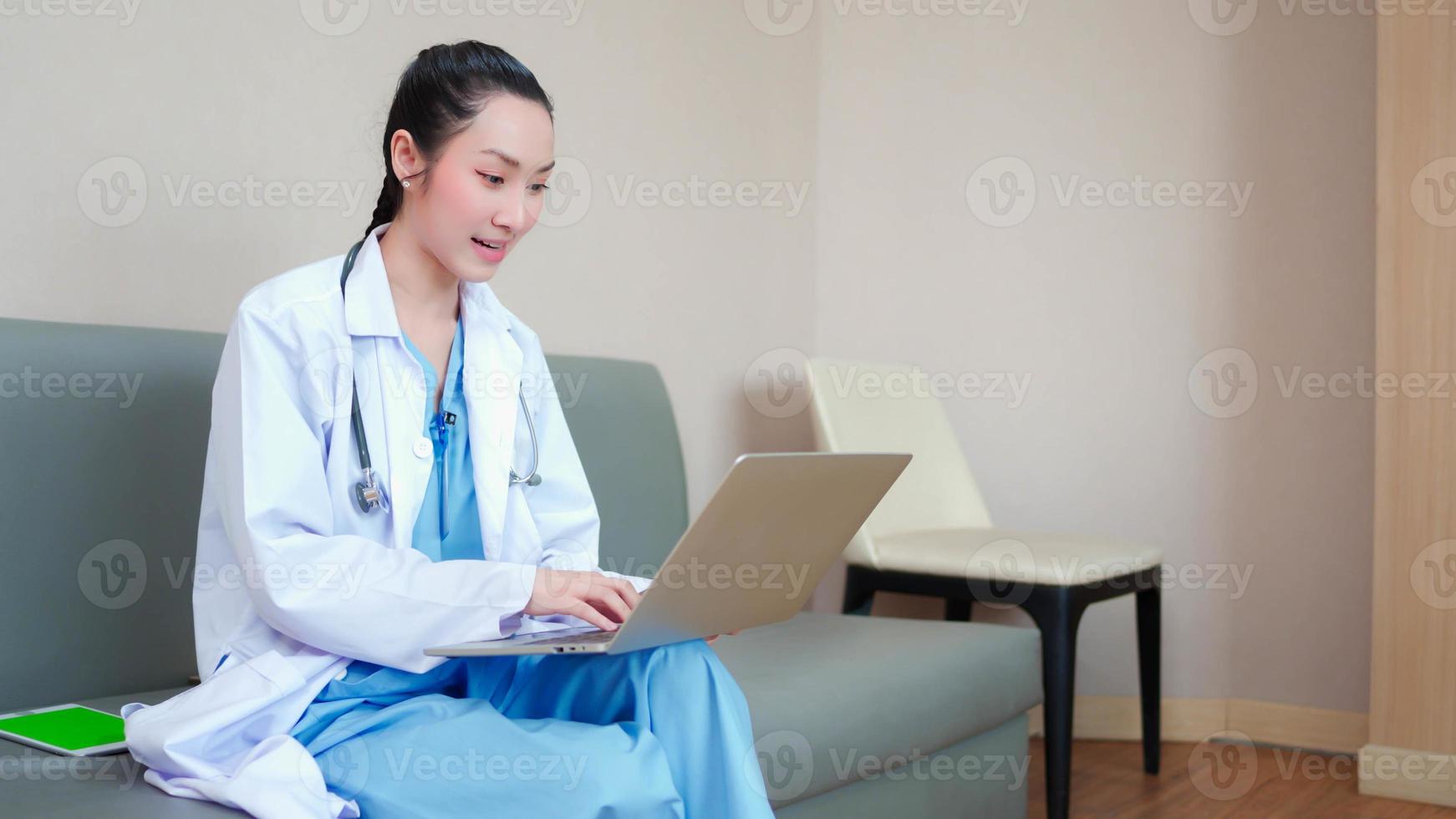 femme médecin asiatique attrayante et professionnelle en blouse médicale blanche. tout en étant assis sur un canapé, en faisant une conférence vidéo sur un ordinateur portable, en consultant un patient à distance en ligne. concept de soins de santé de télémédecine. photo