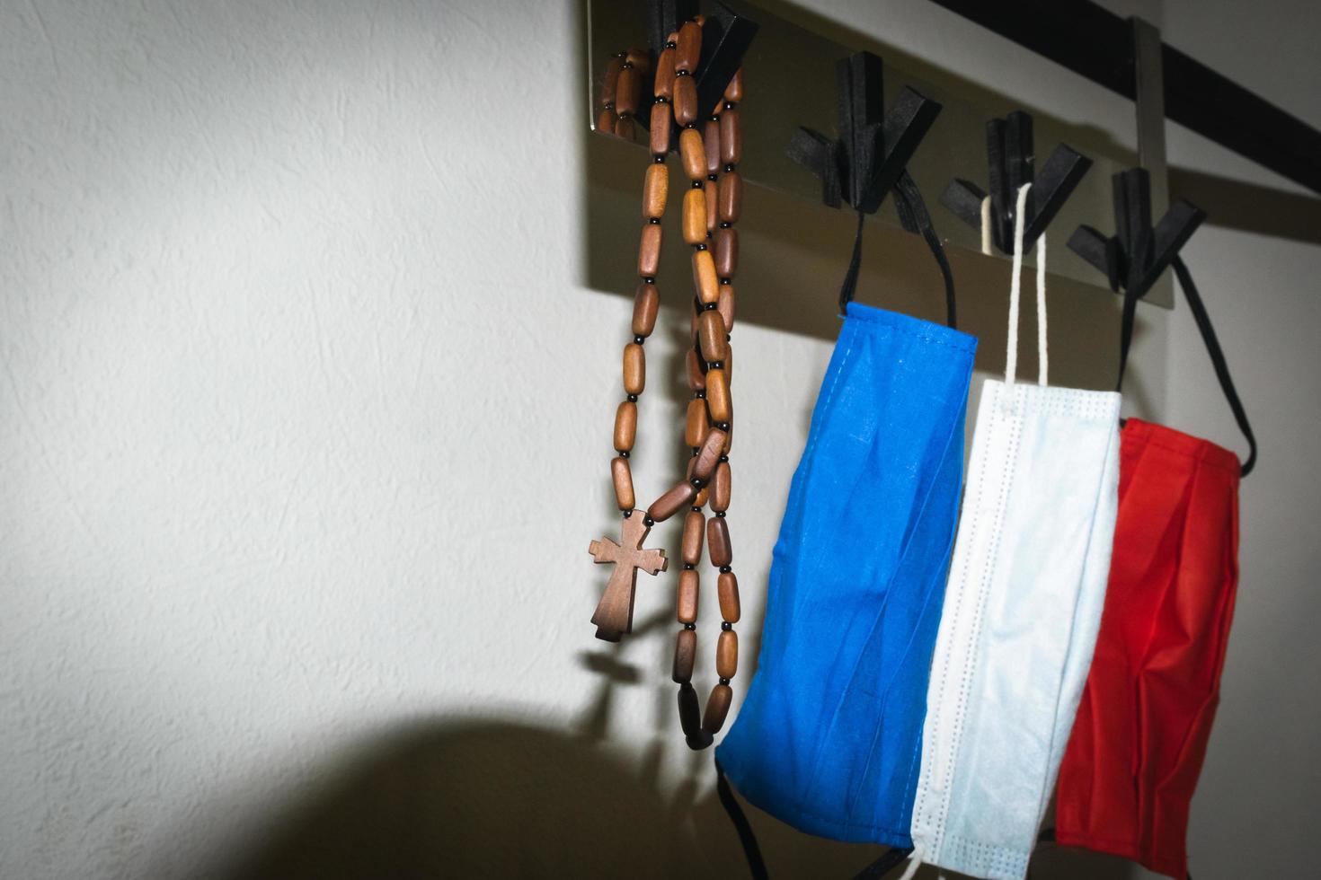 chapelet catholique en bois marron et trois masques faciaux suspendus à des crochets à la maison photo