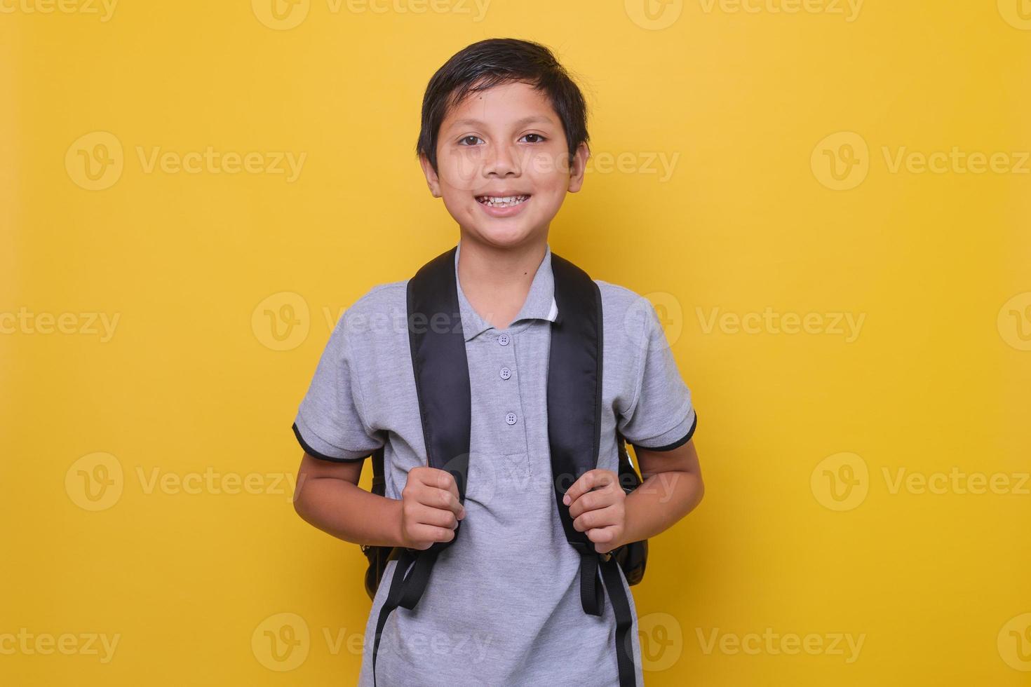écolier asiatique dans un style décontracté avec sac à dos noir sourit isolé sur fond jaune. concept de retour à l'école. photo