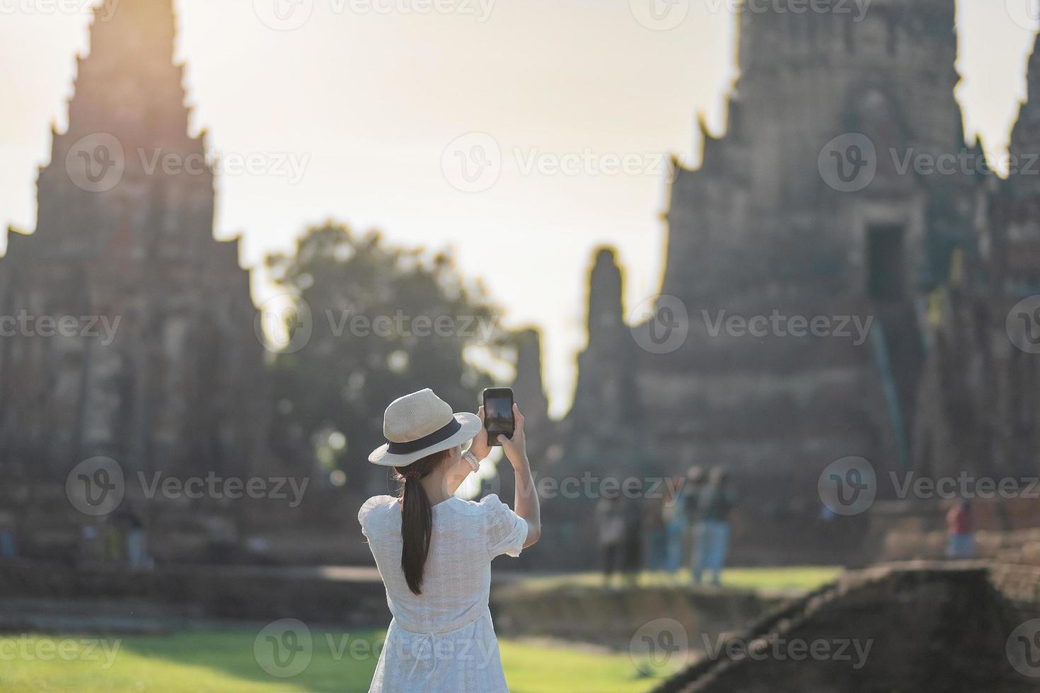 femme touristique heureuse en robe blanche prenant une photo par smartphone mobile, lors de la visite du temple wat chaiwatthanaram dans le parc historique d'ayutthaya, été, solo, concept de voyage en asie et en thaïlande