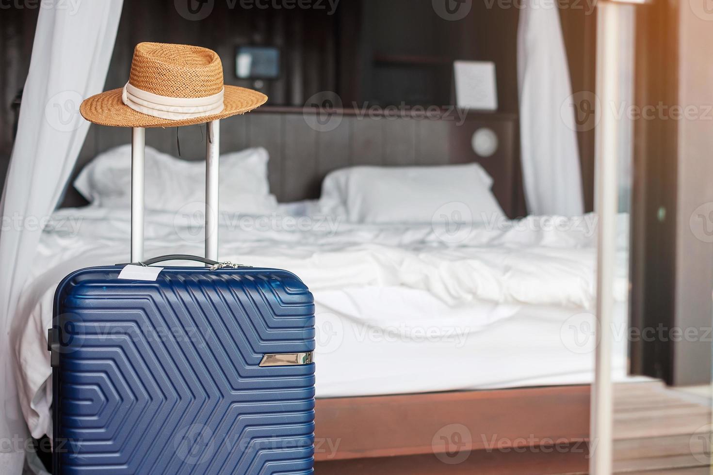 bagages bleus avec chapeau dans une chambre d'hôtel moderne après l'ouverture de la porte. temps de voyager, service, voyage, voyage, vacances d'été et concepts de vacances photo