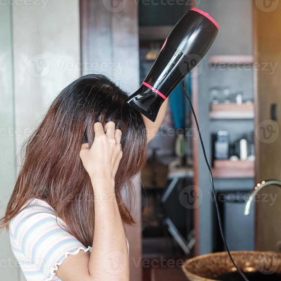 jeune femme utilisant un sèche-cheveux près d'un miroir à la maison ou à l'hôtel. coiffures et concepts de style de vie photo