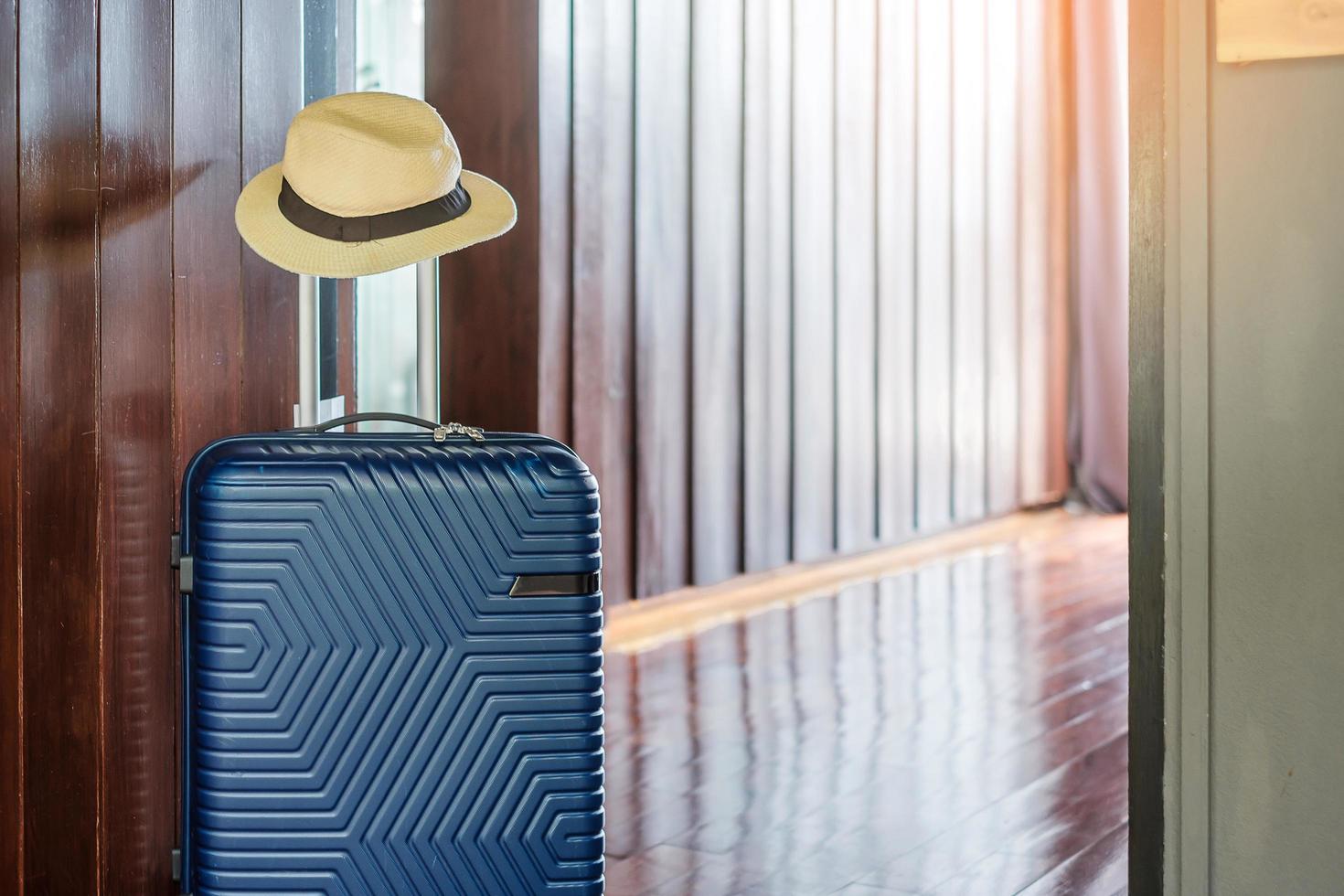 bagages bleus avec chapeau dans une chambre d'hôtel moderne après l'ouverture de la porte. temps de voyager, service, voyage, voyage, vacances d'été et concepts de vacances photo