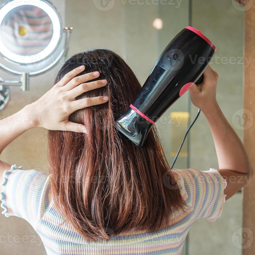 jeune femme utilisant un sèche-cheveux près d'un miroir à la maison ou à l'hôtel. coiffures et concepts de style de vie photo