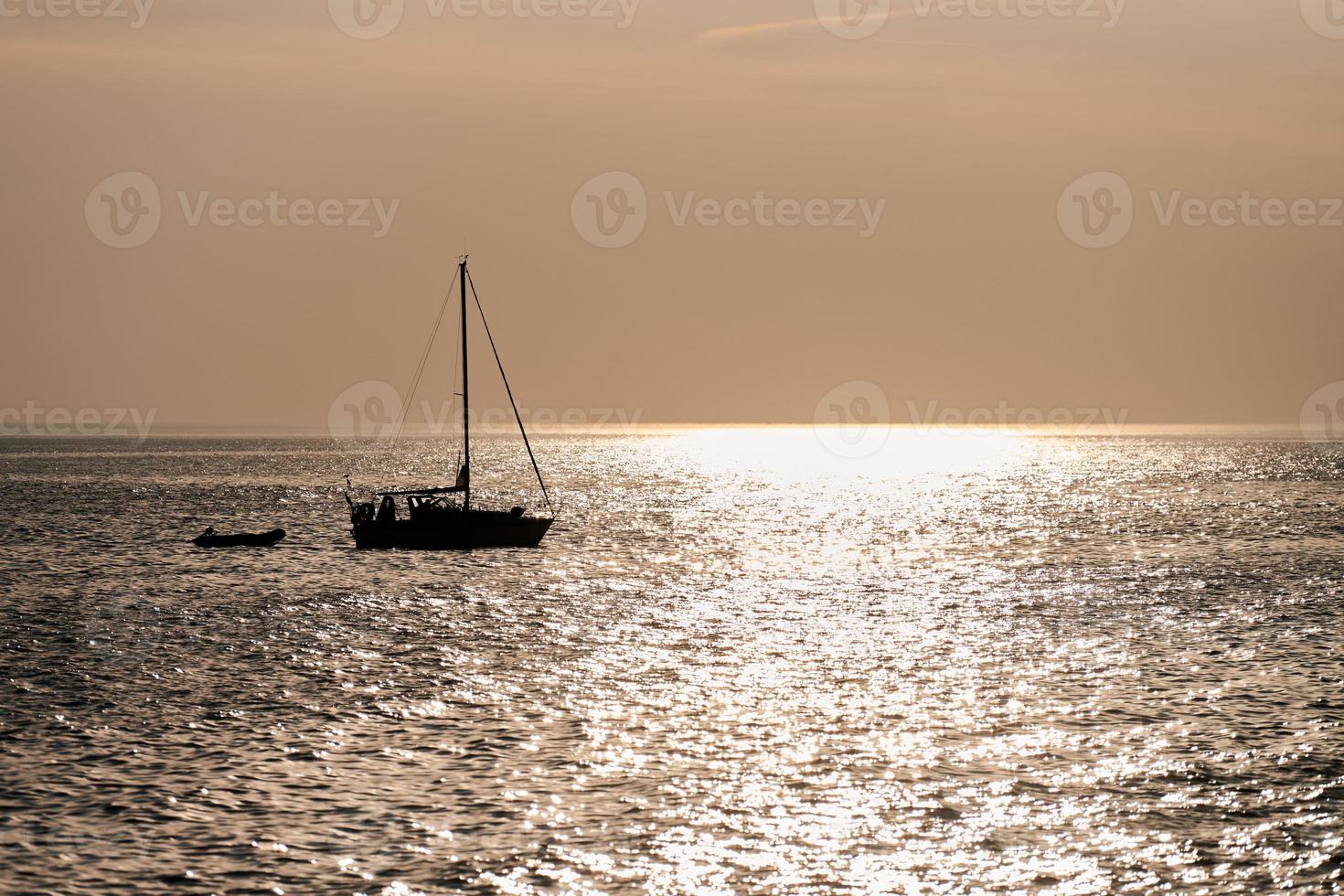 deux voiliers silhouettes sur fond de beau coucher de soleil avec reflet dans l'eau de mer calme photo