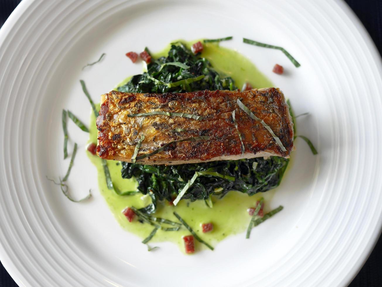 gros plan directement au-dessus de la vue de la tranche de bar grillé sur les épinards dans une assiette blanche, menu de cuisine gastronomique photo