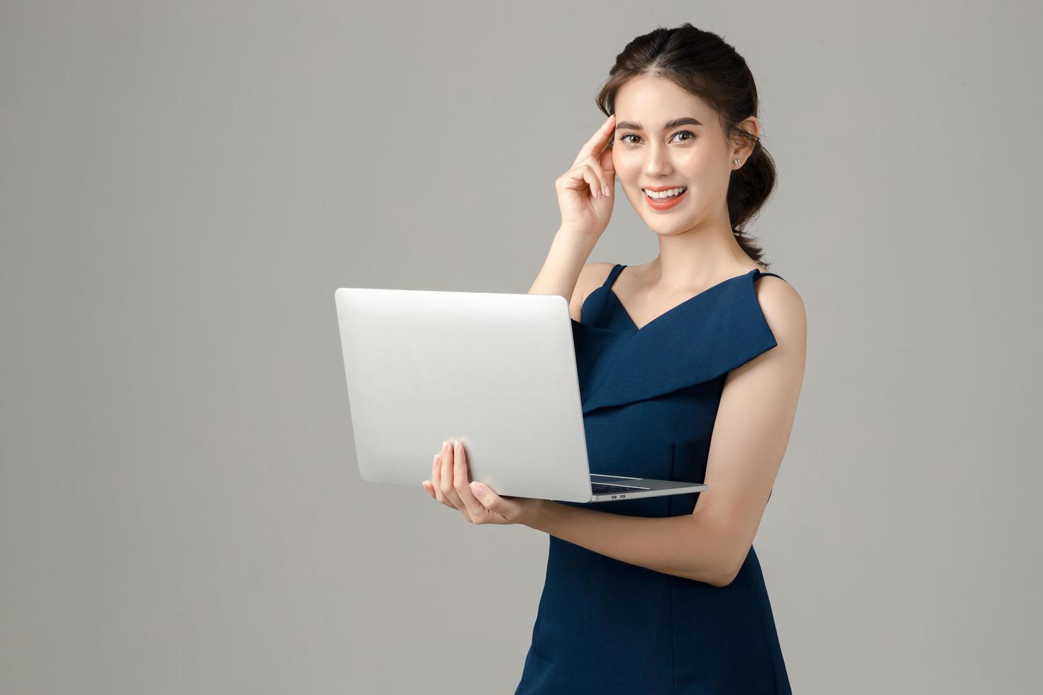 jeune femme d'affaires asiatique énergique tenant un ordinateur portable et pensant sur fond gris. portrait de jolie fille en studio. petite entreprise PME, freelance en ligne, concept de commerce électronique. photo