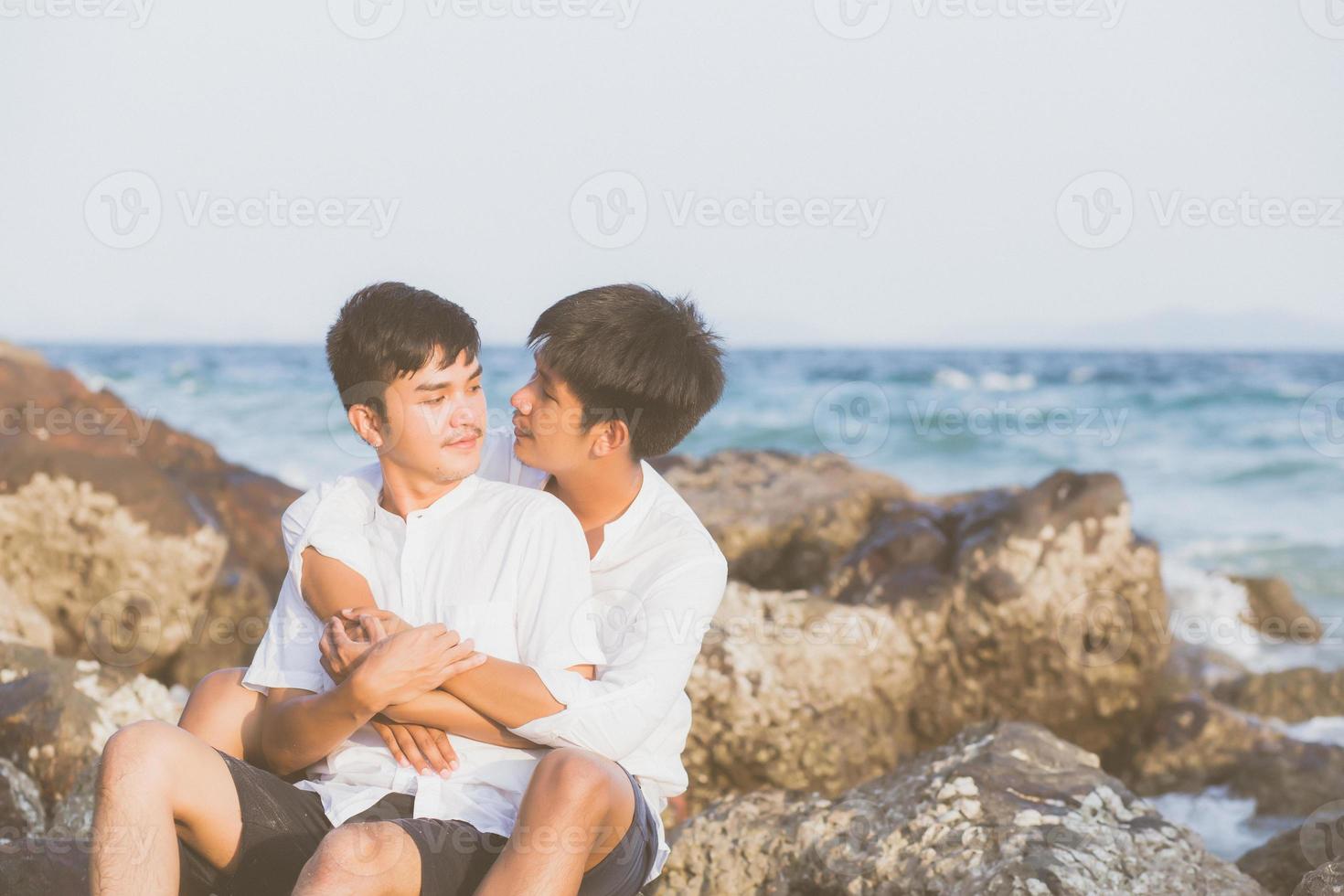 portrait homosexuel jeune couple asiatique assis câlin ensemble sur un rocher ou une pierre sur la plage en été, asie gay faisant du tourisme pour les loisirs et se détendre avec plaisir en vacances en mer, concept juridique lgbt. photo