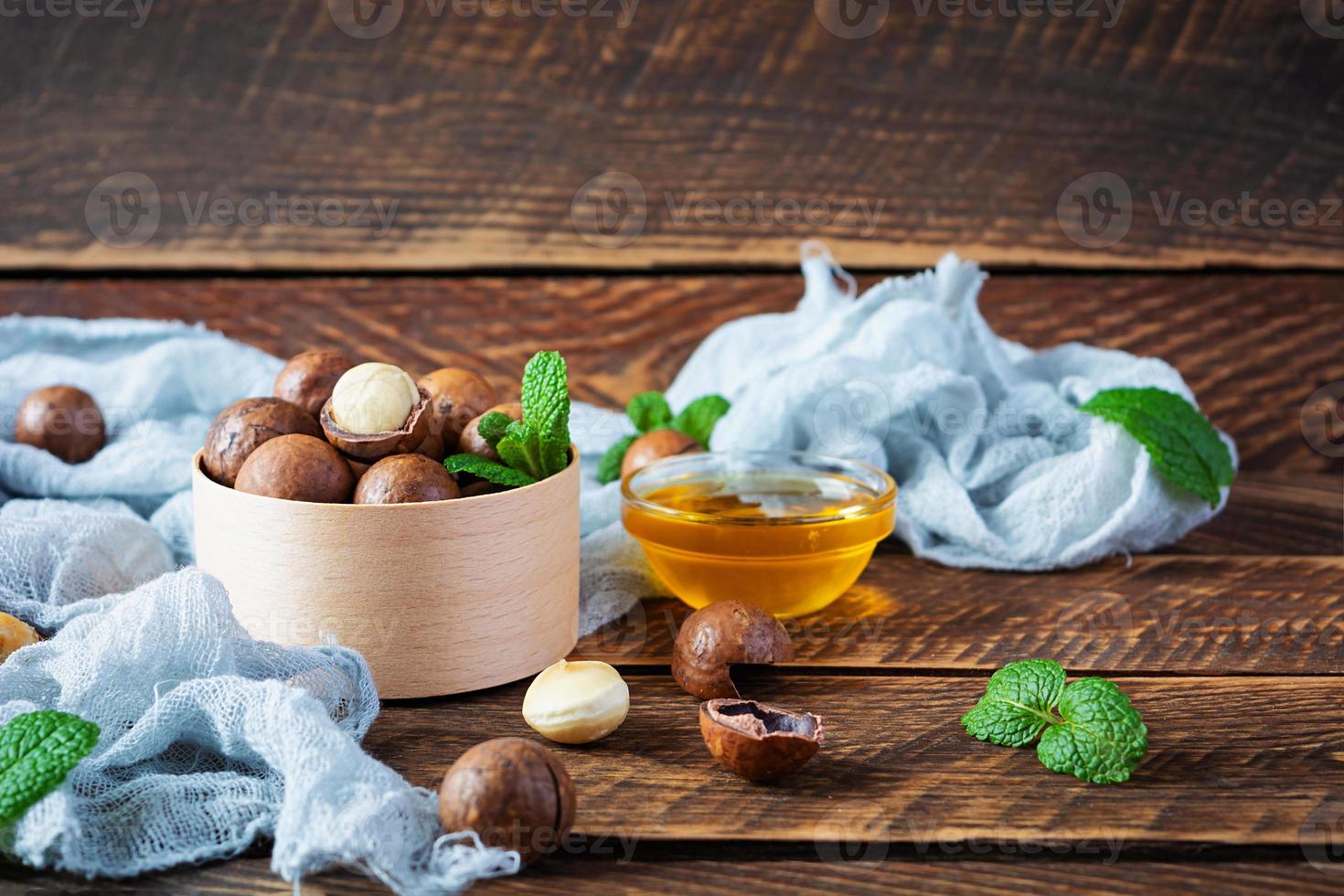 Noix de macadamia en coquille avec des feuilles de menthe et du miel sur fond de bois photo