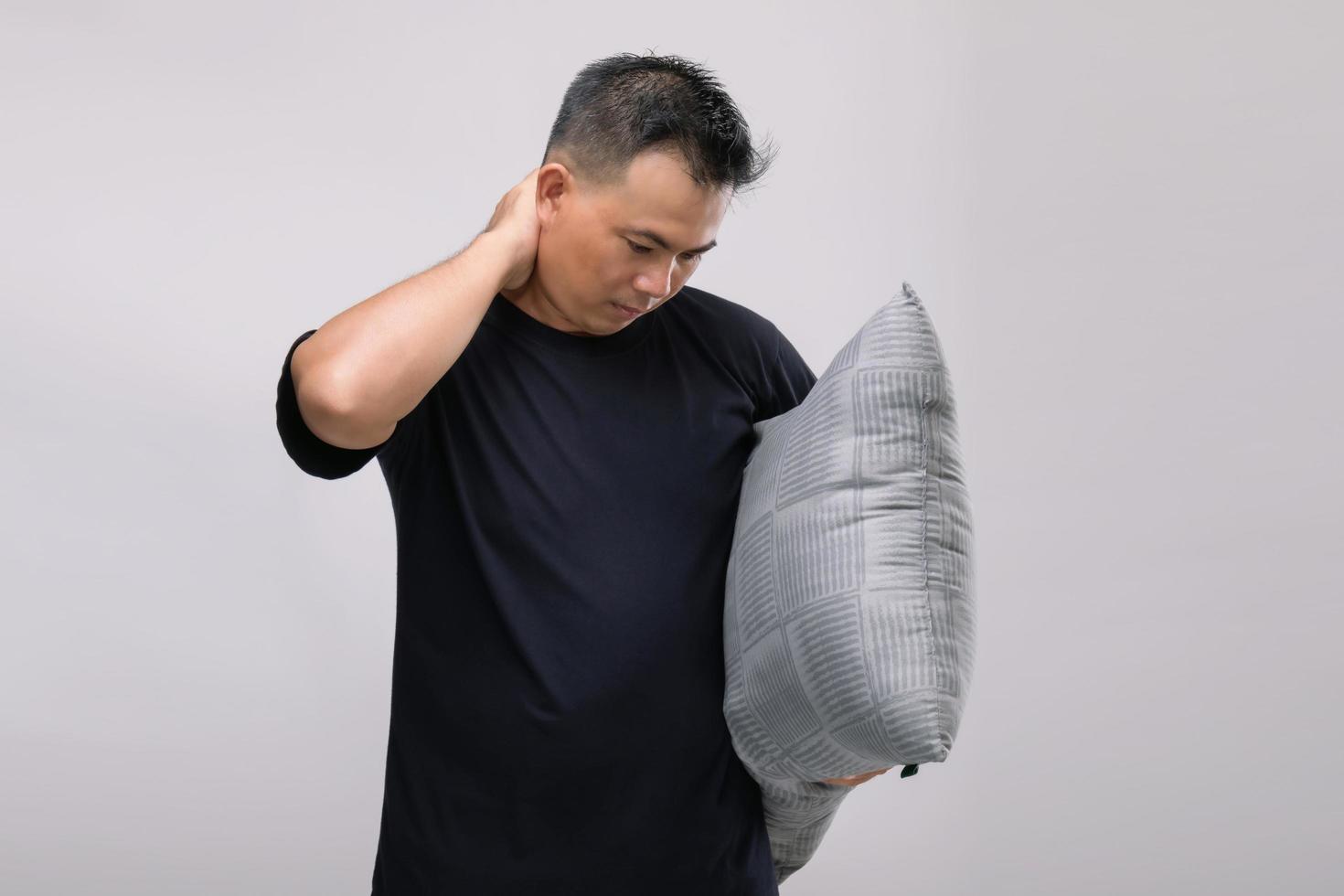 concept de maux de cou, portrait d'un homme asiatique tenant un oreiller gris et se sentant fatigué ou souffrant de douleurs au cou. tourné en studio isolé sur gris photo