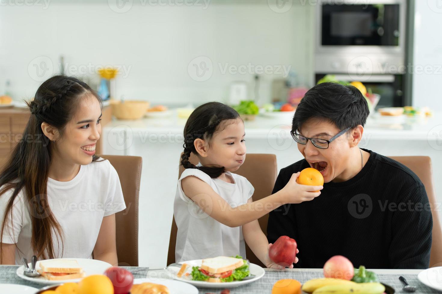 père et mère asiatiques montrent votre amour à la petite fille et prennent le petit déjeuner ensemble joyeusement dans la salle à manger de la maison. photo