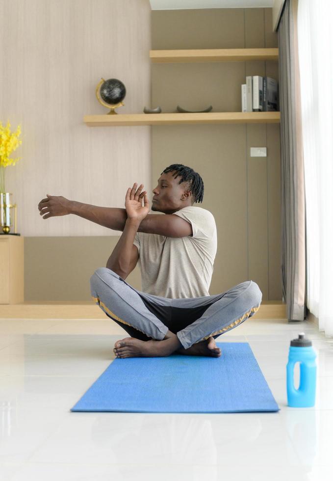 jeune homme africain faisant de l'exercice de yoga dans le salon de sa maison avec le plaisir de se détendre avec des sports légers dans l'atmosphère matinale de la journée. photo