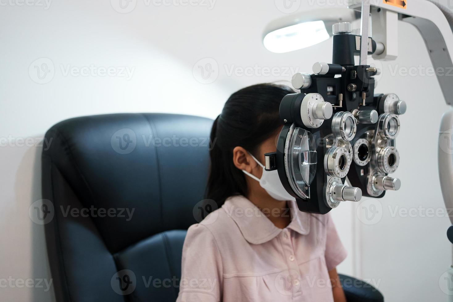 ophtalmologiste examinant les yeux d'une fille asiatique dans une clinique. ils portent des masques protecteurs. photo