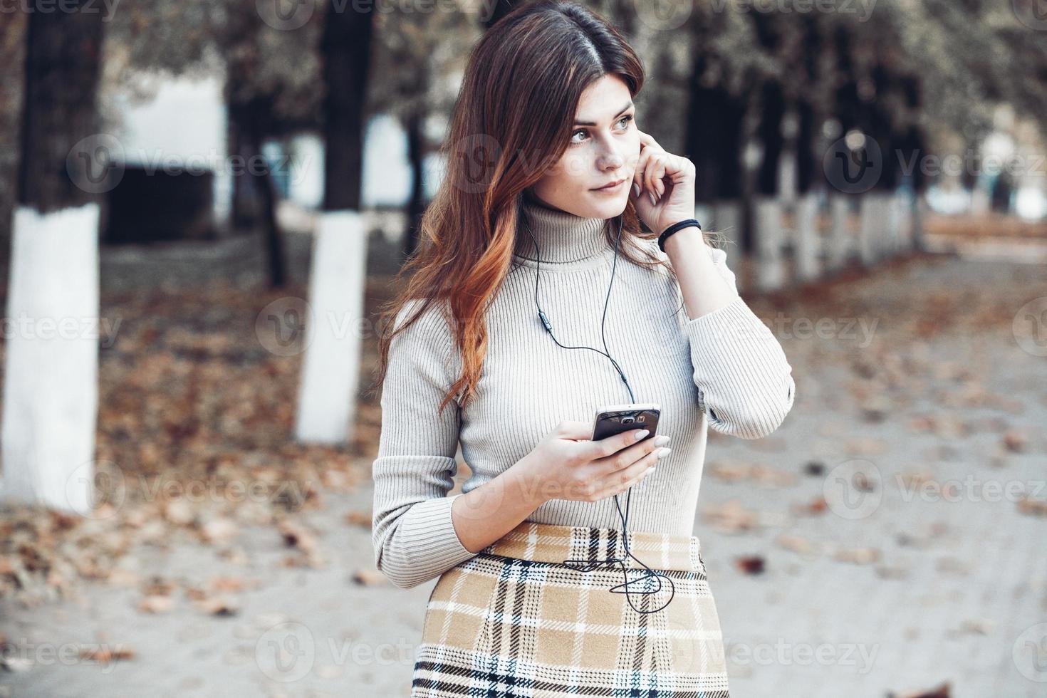 image de belle femme élégante tenant un téléphone portable. jeune fille européenne debout dans la rue et utilisant un téléphone portable. femme écoutant de la musique avec le téléphone et s'amusant. notion d'internet mobile. photo